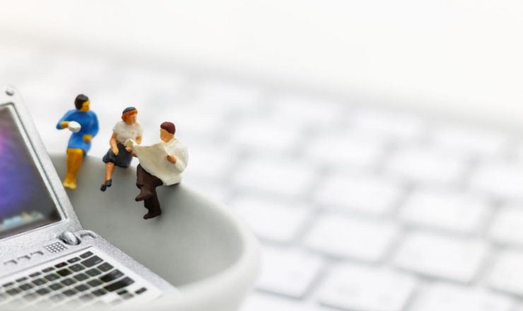 ノートパソコンの上に配置された3つのミニチュアフィギュア。キーボードを背景に、ビジネスの会話や取引をしているような様子