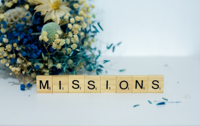 企業理念・ミッション | 青と黄色の花とスクラブルタイルで表現されたMISSIONSの文字