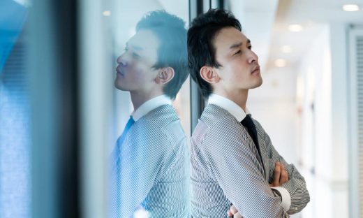 ガラスにもたれかかり、考え込むスーツ姿の男性