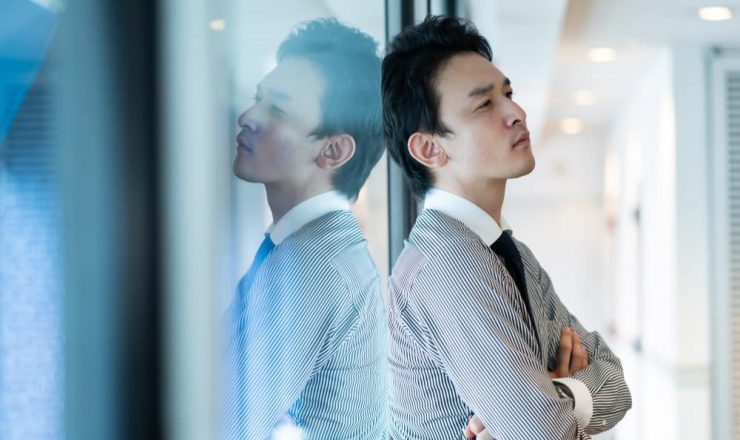 ガラスにもたれかかり、考え込むスーツ姿の男性