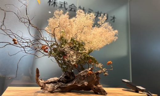 株式会社ミガリオのエントランスに飾られた、スモークツリーとツルウメモドキを使った秋の生け花。流木を土台にダイナミックに活けられている。